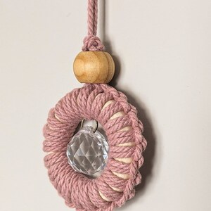 May include: A pink macrame ring with a crystal prism hanging in the centre. The ring is attached to a wooden bead and a pink cord.
