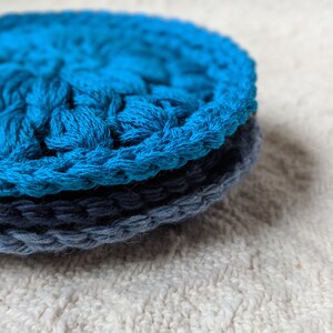 May include: Two crocheted scrubbies, one blue and one dark blue, stacked on top of each other.