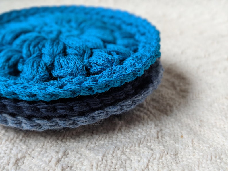 May include: Two crocheted scrubbies, one blue and one dark blue, stacked on top of each other.