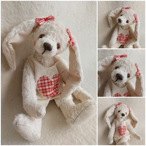 May include: A white plush bunny with floppy ears, wearing a red and white checkered heart on a white dress. The bunny has red bows on its ears.