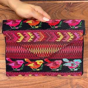May include: A black fabric clutch with a colorful embroidered design featuring birds and geometric patterns. The clutch has a flap closure and a red, pink, and yellow color scheme.