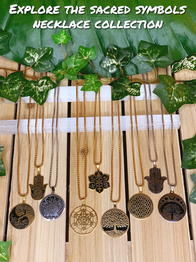 May include: A collection of gold and silver-toned necklaces with various sacred symbols, including a tree of life, lotus flower, and Hamsa hand. The necklaces hang against a wooden background, with the text "EXPLORE THE SACRED SYMBOLS NECKLACE COLLECTION" at the top.