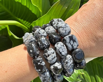 May include: Four stacked bracelets made of black and white snowflake obsidian stones. Each bracelet is made of smooth, rounded stones.
