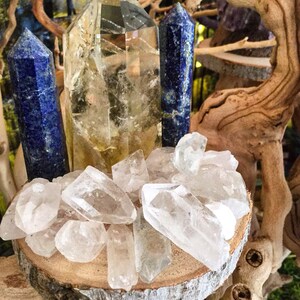 May include: A collection of clear quartz crystals, including a large, clear quartz point, and two blue lapis lazuli points, arranged on a wooden slice.