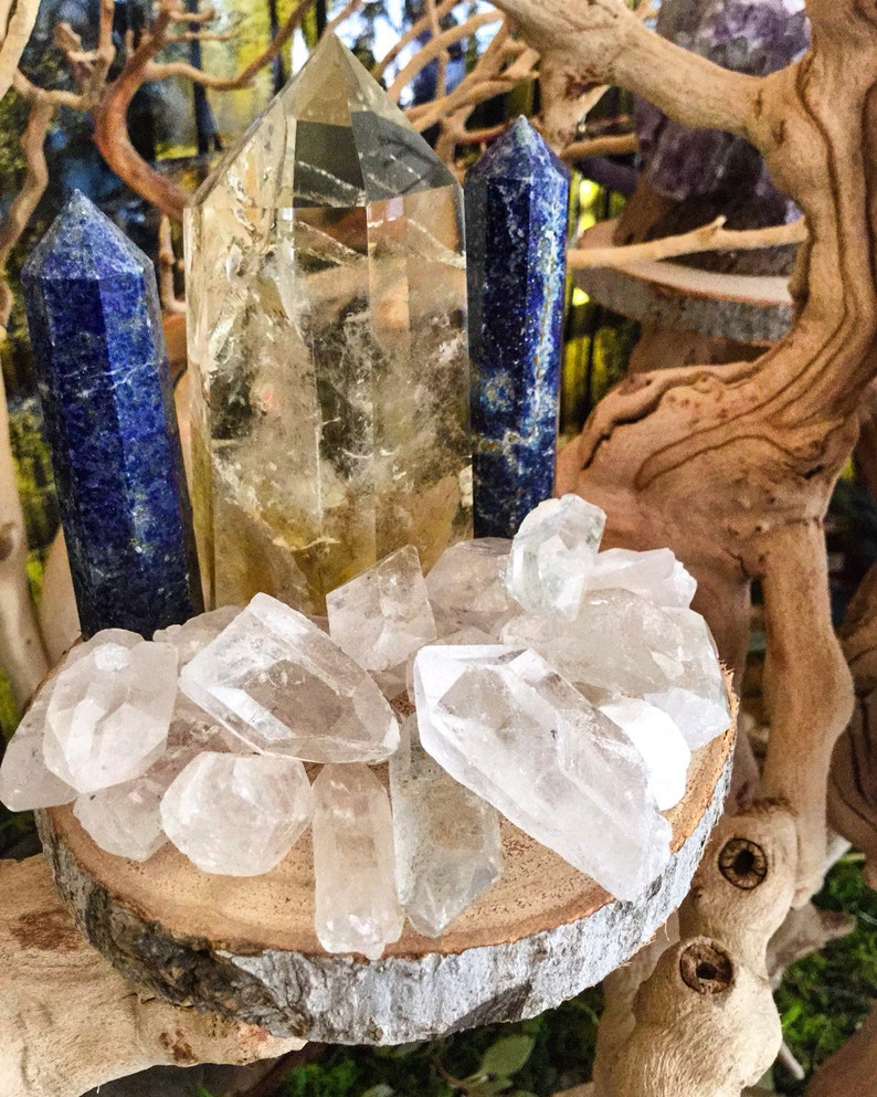 May include: A collection of clear quartz crystals, including a large, clear quartz point, and two blue lapis lazuli points, arranged on a wooden slice.