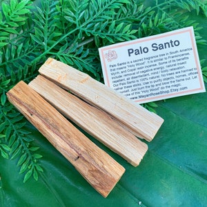 May include: Three brown Palo Santo sticks on a green leafy background. The sticks are used for smudging and cleansing. The text on the card reads "Palo Santo is a sacred fragrance tree in South America that means "Holy Wood". It is similar to Frankincense, Myrrh, and Copal resin incense. Some of its benefits include: removal of negative energy, natural insect repellent, air disinfectant, mind/body relaxation. Our Palo Santo is 100% natural. No trees are harmed to gather these sticks. Use to purify objects, homes, offices or yourself. Just burn the tip and blow the flame out. Let the smoke of this "Holy Wood" do the magic. www.MayanRoseShop.Etsy.com"