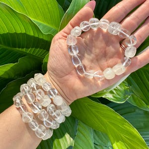 May include: A set of four clear quartz crystal bracelets with smooth, rounded beads. The bracelets are stacked on a person's wrist.