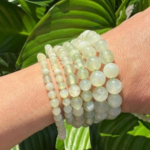 May include: A stack of green jade bracelets with round beads. The bracelets are stacked on a person's wrist.