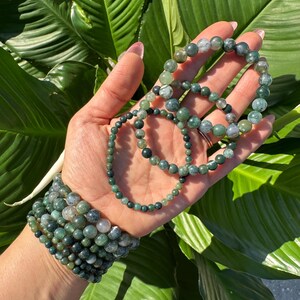 May include: A set of green agate beaded bracelets with varying sizes and patterns. The bracelets are stacked on a person's wrist.