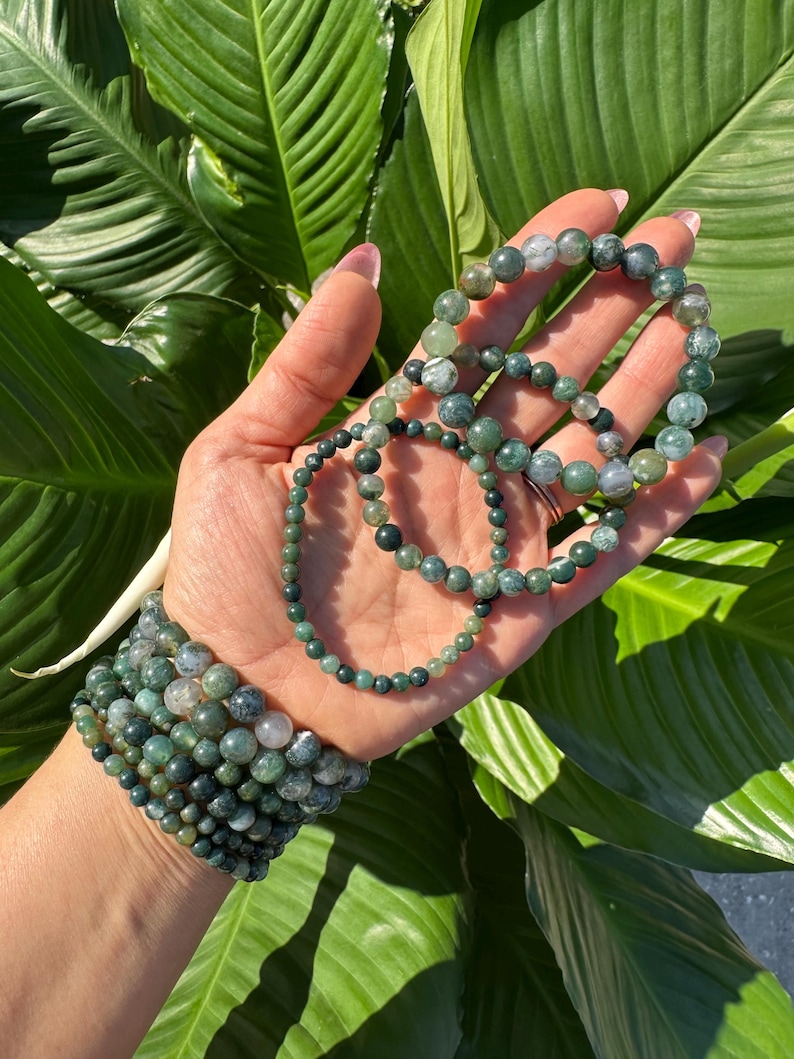 May include: A set of green agate beaded bracelets with varying sizes and patterns. The bracelets are stacked on a person's wrist.