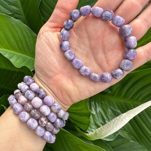 Puede incluir: Un conjunto de cuatro pulseras de piedras preciosas moradas con cuentas redondas. Las pulseras est&aacute;n apiladas en la mu&ntilde;eca de una persona.