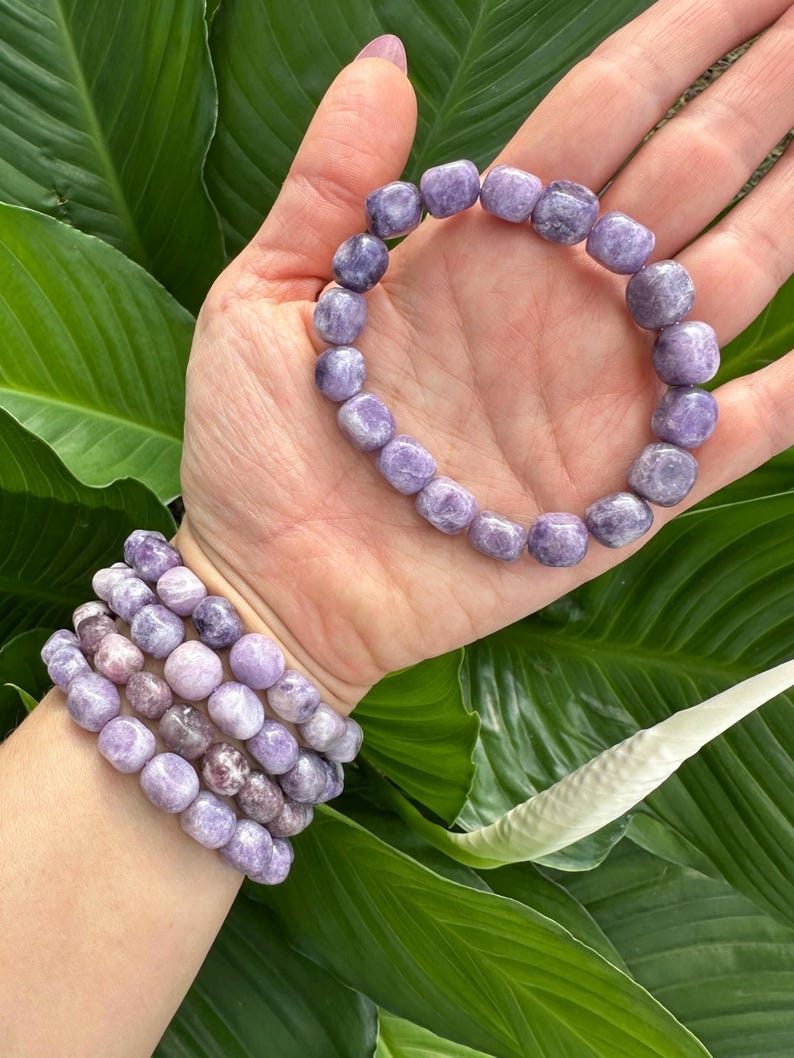 Puede incluir: Un conjunto de cuatro pulseras de piedras preciosas moradas con cuentas redondas. Las pulseras est&aacute;n apiladas en la mu&ntilde;eca de una persona.