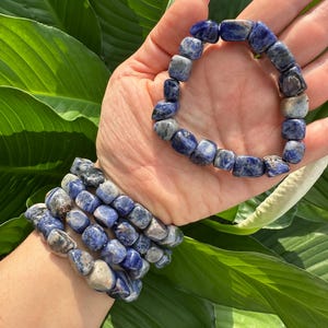 Peut inclure: Un ensemble de cinq bracelets en pierres pr&eacute;cieuses bleues et blanches. Les bracelets sont faits de pierres roul&eacute;es et sont empil&eacute;s sur le poignet d'une personne.