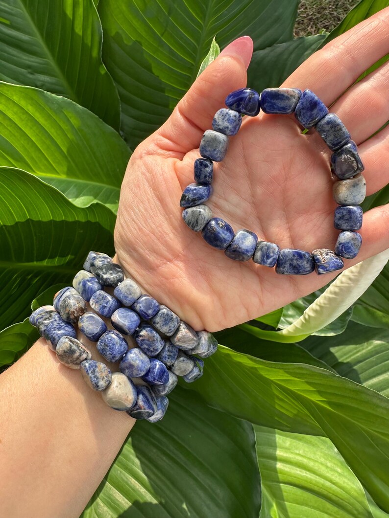 Peut inclure: Un ensemble de cinq bracelets en pierres pr&eacute;cieuses bleues et blanches. Les bracelets sont faits de pierres roul&eacute;es et sont empil&eacute;s sur le poignet d'une personne.