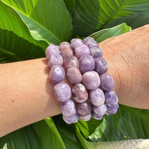 Puede incluir: Un brazalete hecho de m&uacute;ltiples hebras de cuentas de piedra preciosa de amatista lavanda. Las cuentas son lisas y redondas, y est&aacute;n dispuestas en un patr&oacute;n apilado. El brazalete se lleva en la mu&ntilde;eca.