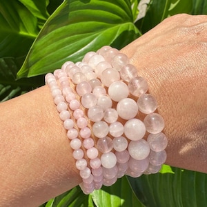 Puede incluir: Un conjunto de pulseras de cuarzo rosa de diferentes tamaños de cuentas. Las pulseras se llevan en la muñeca.