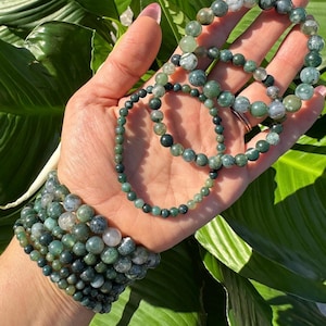 May include: A set of green agate beaded bracelets with varying sizes and patterns. The bracelets are stacked on a person's wrist.