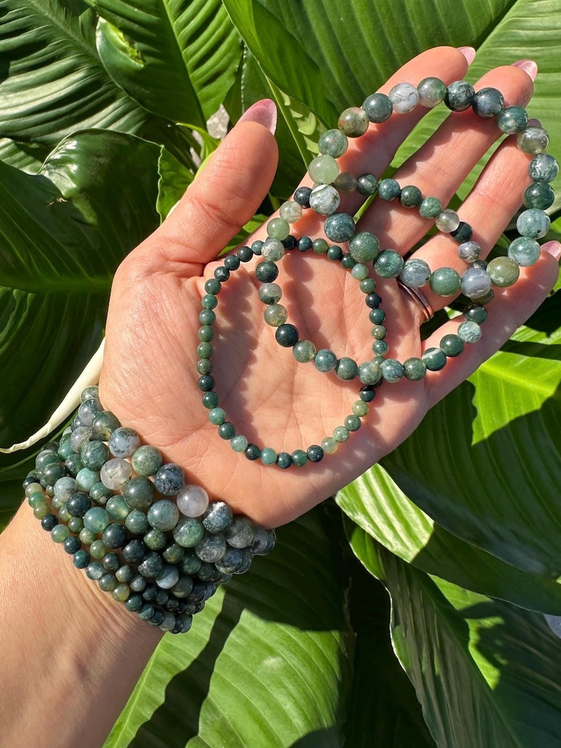 May include: A set of green agate beaded bracelets with varying sizes and patterns. The bracelets are stacked on a person's wrist.