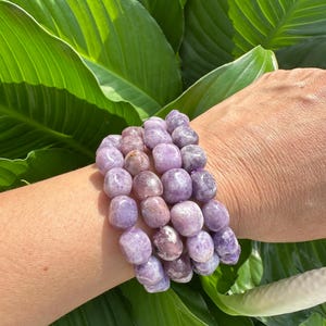 Puede incluir: Un conjunto de cuatro pulseras hechas con cuentas de piedra preciosa de lepidolita p&uacute;rpura y rosa. Las pulseras se llevan en la mu&ntilde;eca.