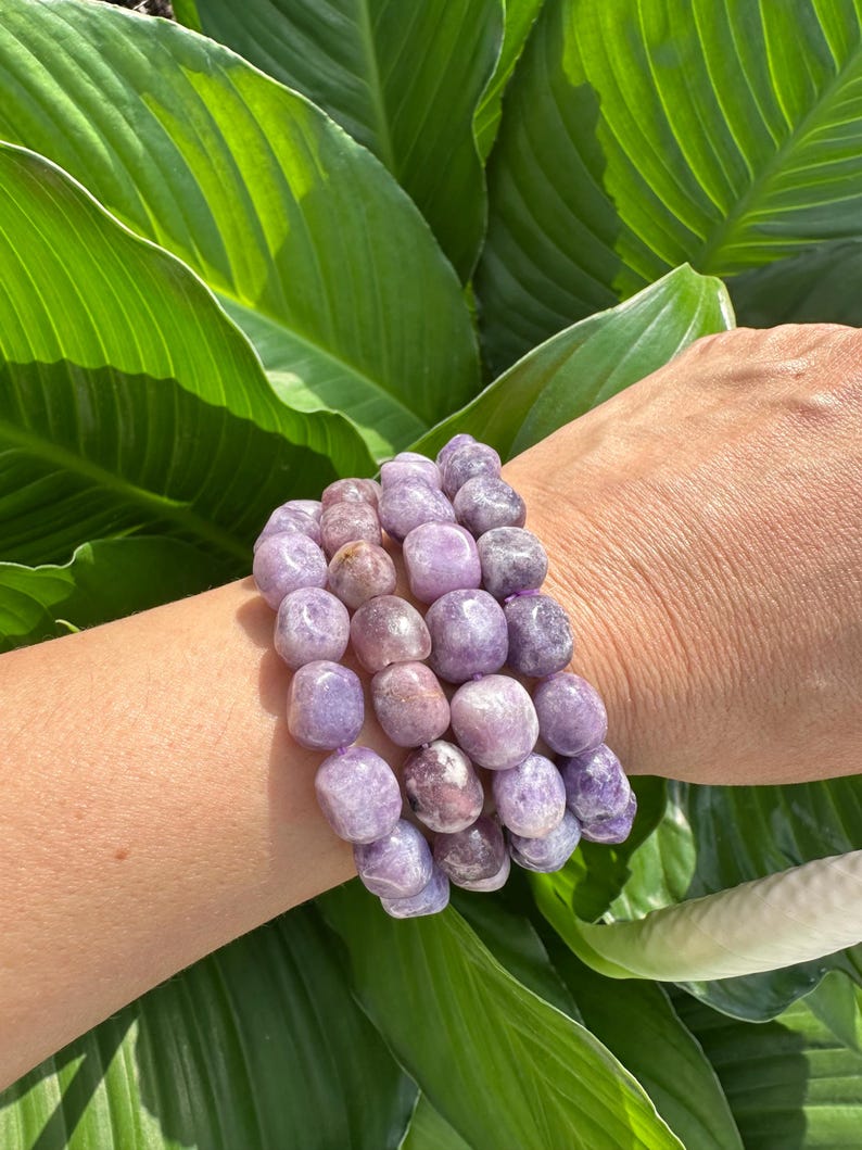 Puede incluir: Un conjunto de cuatro pulseras hechas con cuentas de piedra preciosa de lepidolita p&uacute;rpura y rosa. Las pulseras se llevan en la mu&ntilde;eca.