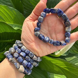 Peut inclure: Un ensemble de bracelets en pierres bleues et blanches, avec un seul bracelet port&eacute; au poignet. Les bracelets sont faits de pierres roul&eacute;es.