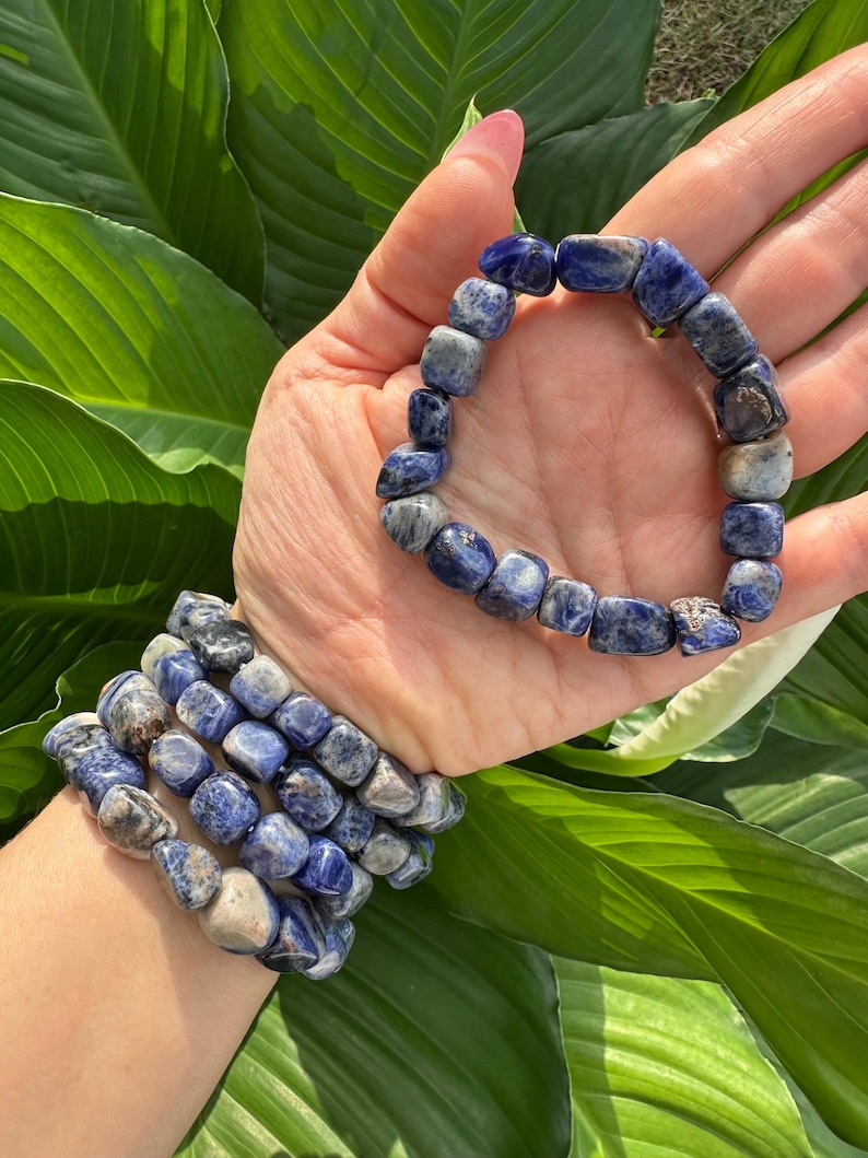 Peut inclure: Un ensemble de bracelets en pierres bleues et blanches, avec un seul bracelet port&eacute; au poignet. Les bracelets sont faits de pierres roul&eacute;es.