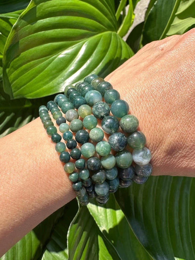 May include: A stack of green agate beaded bracelets. The bracelets are made of round, smooth beads with a variety of green shades and patterns.