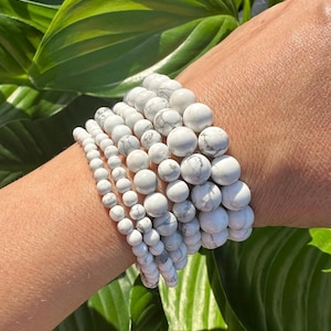 May include: A stack of white howlite beaded bracelets. The bracelets are made of smooth, round beads with a marbled pattern.