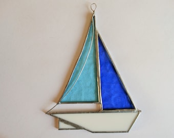 May include: A stained glass sailboat ornament with a blue and white sail and a white hull.