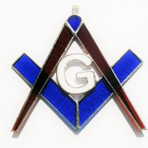 Könnte beinhalten: Ein hängendes Buntglasfenster mit einem blauen und roten Freimaurersymbol, ein Quadrat und ein Zirkel mit einem weißen Buchstaben G in der Mitte.