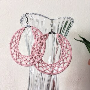 K&ouml;nnte beinhalten: Ein Paar rosafarbene geh&auml;kelte Creolen mit silbernen Haken. Die Ohrringe h&auml;ngen an einer Glasvase.