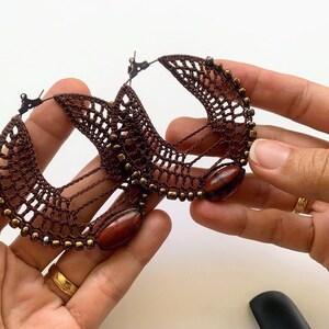 以下が含まれることがあります： 茶色のクロシェのフープイヤリングのペア。茶色の木製ビーズと金のアクセントが施されています。