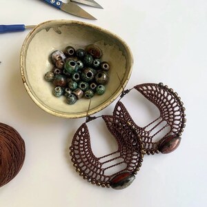 以下が含まれることがあります： 茶色のクロシェのフープイヤリングに、茶色と緑のビーズがついたペア。イヤリングは手作りで、ユニークなデザインです。