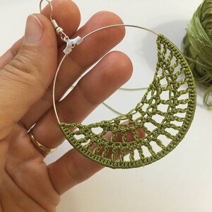 K&ouml;nnte beinhalten: Ein Paar gr&uuml;ne H&auml;kelohrringe mit einem silbernen Ring und Haken. Die Ohrringe sind handgefertigt und haben ein zartes, filigranes Design.
