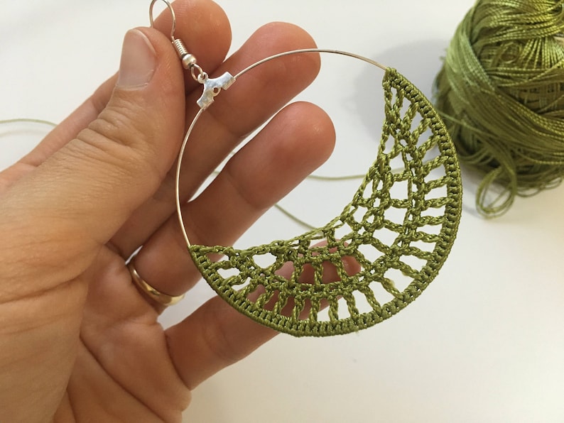 K&ouml;nnte beinhalten: Ein Paar gr&uuml;ne H&auml;kelohrringe mit einem silbernen Ring und Haken. Die Ohrringe sind handgefertigt und haben ein zartes, filigranes Design.