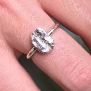 Puede incluir: Un anillo de plata con una banda ovalada texturizada. La banda está martillada y tiene un aspecto rugoso y orgánico.