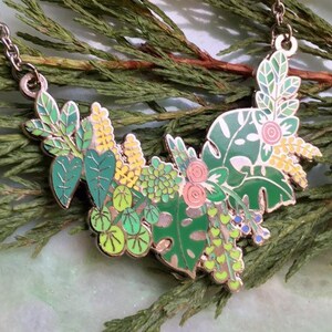 May include: A silver chain necklace with a green, yellow, and pink enamel pendant featuring a cluster of stylized leaves and flowers.