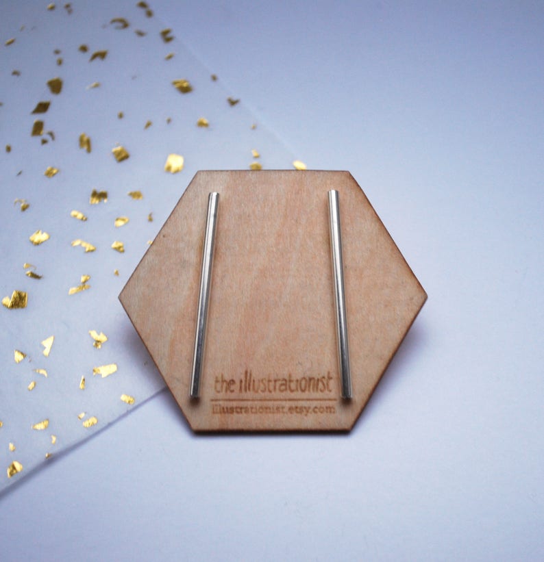 May include: A pair of silver bar earrings displayed on a hexagonal wooden stand. The stand has the text "the illustrationist" and "illustrationist.etsy.com" printed on it.