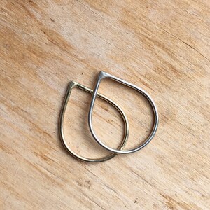 Op de afbeelding: Twee traanvormige oorbellen, een gouden en een zilveren, worden getoond op een houten oppervlak.
