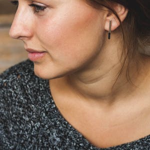 May include: A woman with brown hair wearing a gray sweater and a silver bar earring.