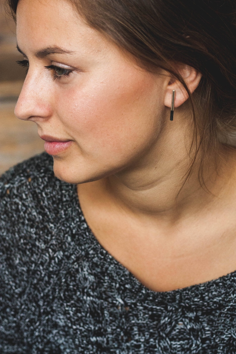 May include: A woman with brown hair wearing a gray sweater and a silver bar earring.