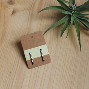 May include: A pair of silver stud earrings with black accents on a brown card with a yellow stripe.