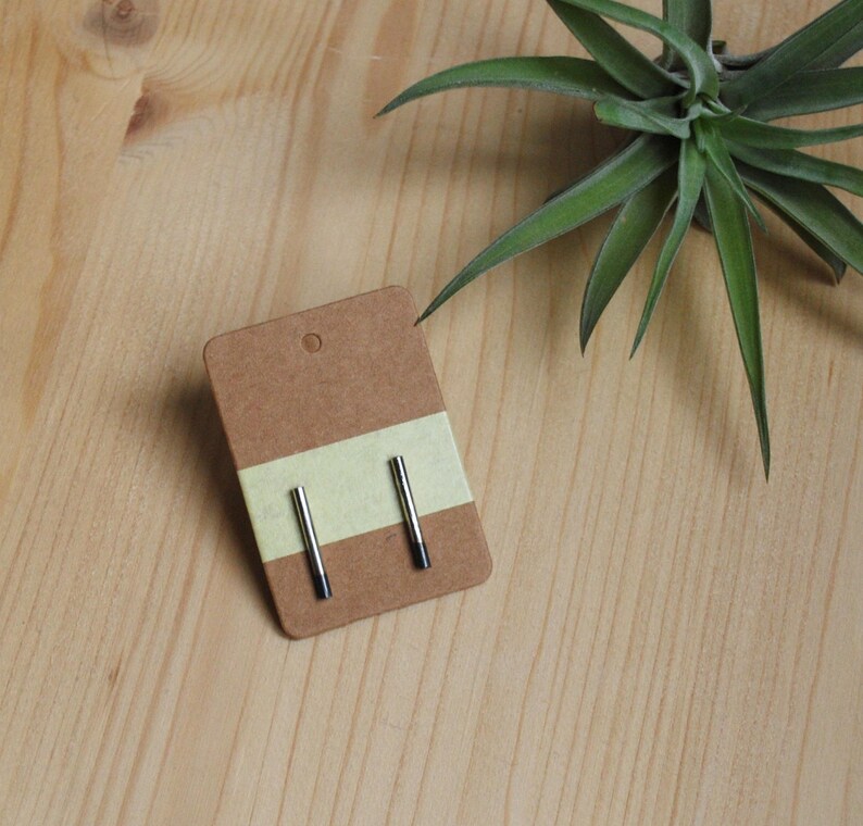 May include: A pair of silver stud earrings with black accents on a brown card with a yellow stripe.