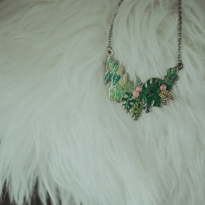 May include: A silver necklace with a green and pink enamel pendant featuring a cluster of leaves and flowers.