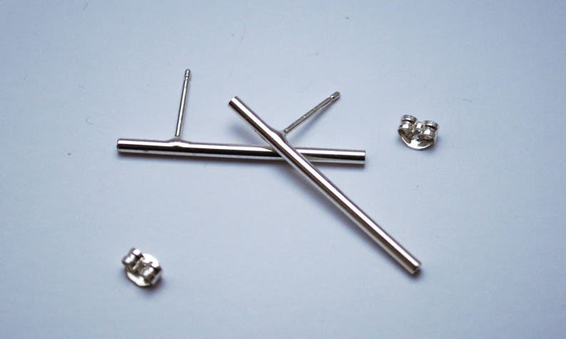May include: A pair of silver bar earrings with post and butterfly back closures. The earrings are simple and modern in design.