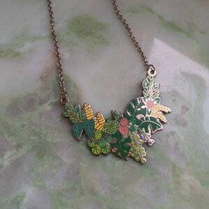 May include: A silver chain necklace with a green, yellow, and pink enamel pendant featuring a cluster of stylized leaves and flowers.