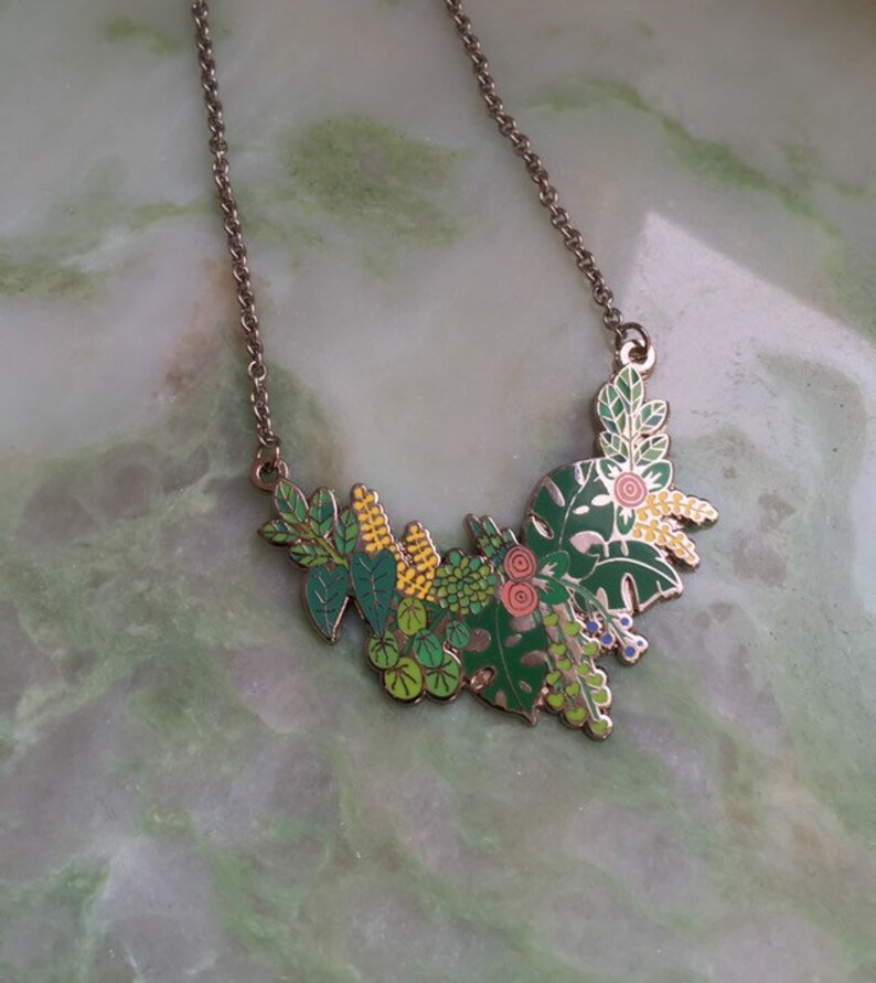 May include: A silver chain necklace with a green, yellow, and pink enamel pendant featuring a cluster of stylized leaves and flowers.