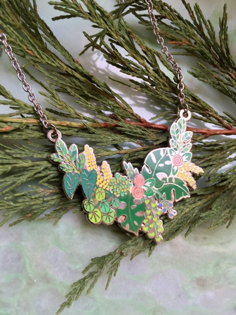 May include: A silver chain necklace with a green, yellow, and pink enamel pendant featuring a cluster of stylized leaves and flowers.