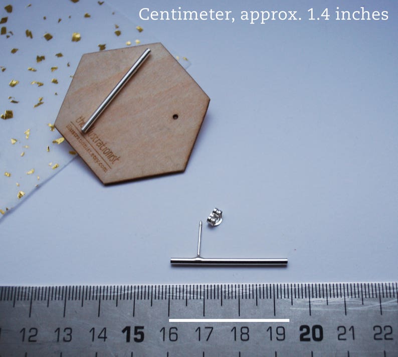 May include: A pair of silver bar earrings, measuring 1.4 inches in length. The earrings are shown on a wooden surface with a ruler for size reference. The ruler shows measurements in centimeters.
