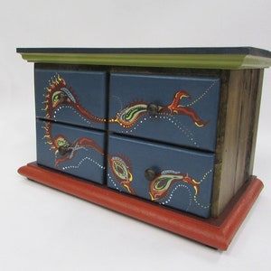 May include: A wooden jewelry box with four drawers painted blue and decorated with colorful paisley designs. The box has a red base and a green top.